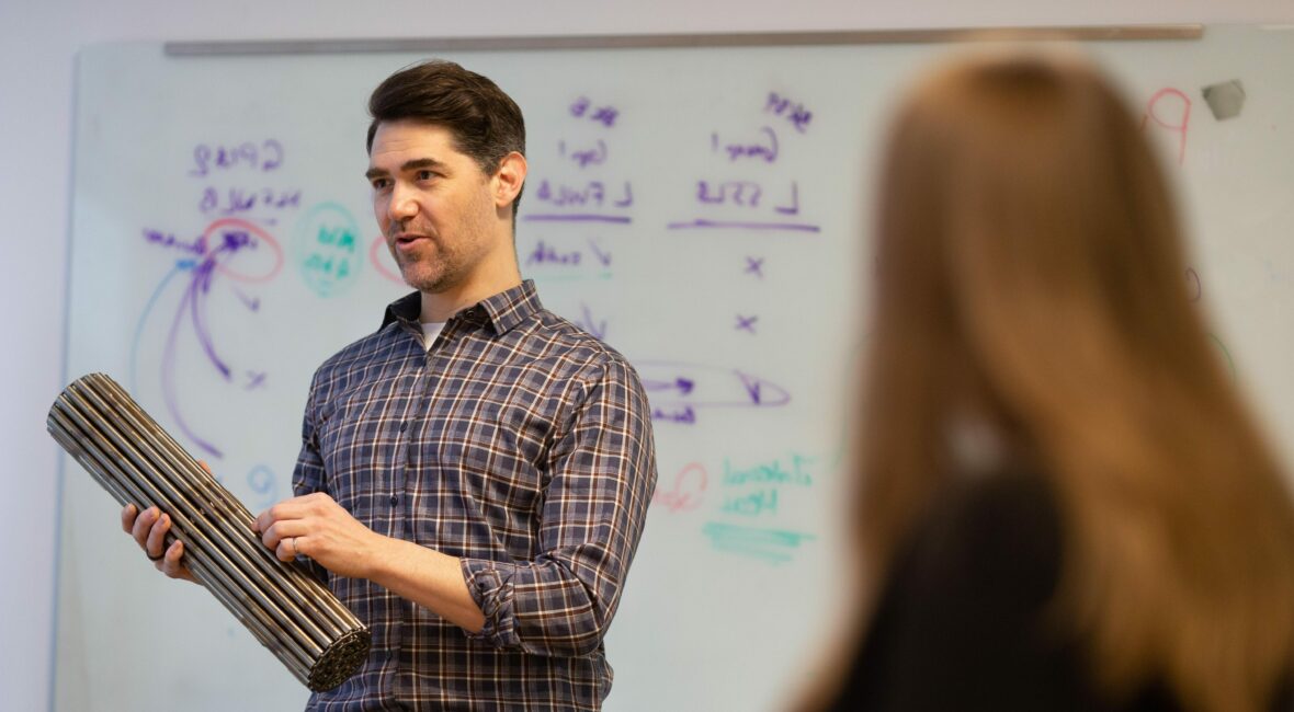 Person teaching audience while holding machine part