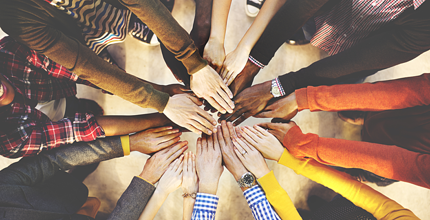 Group of people standing in a circle placing their hands together in a large cheer