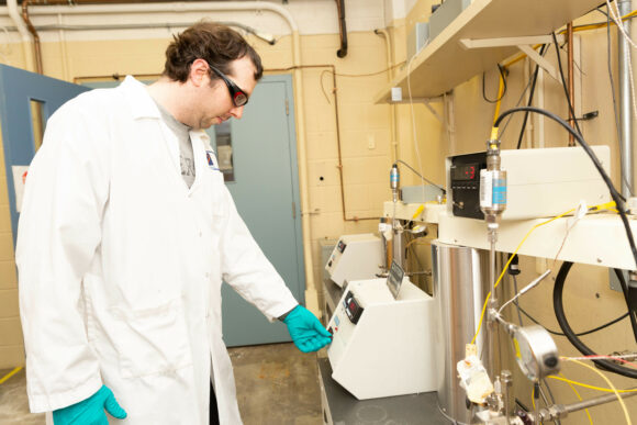 Worker wearing protective equipment operating corrosion testing equipment