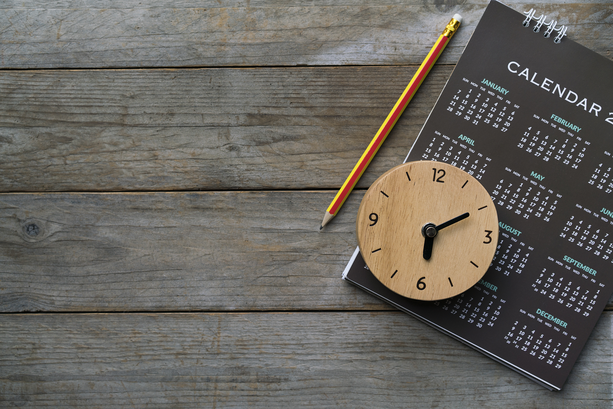 Photograph of a wooden table showcasing a pencil, clock, and calendar